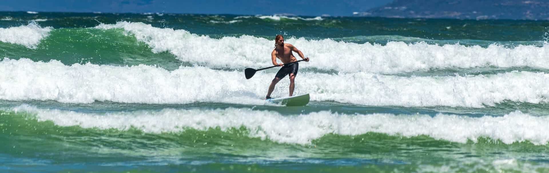 A person paddle boarding through ocean waves on a sunny day.