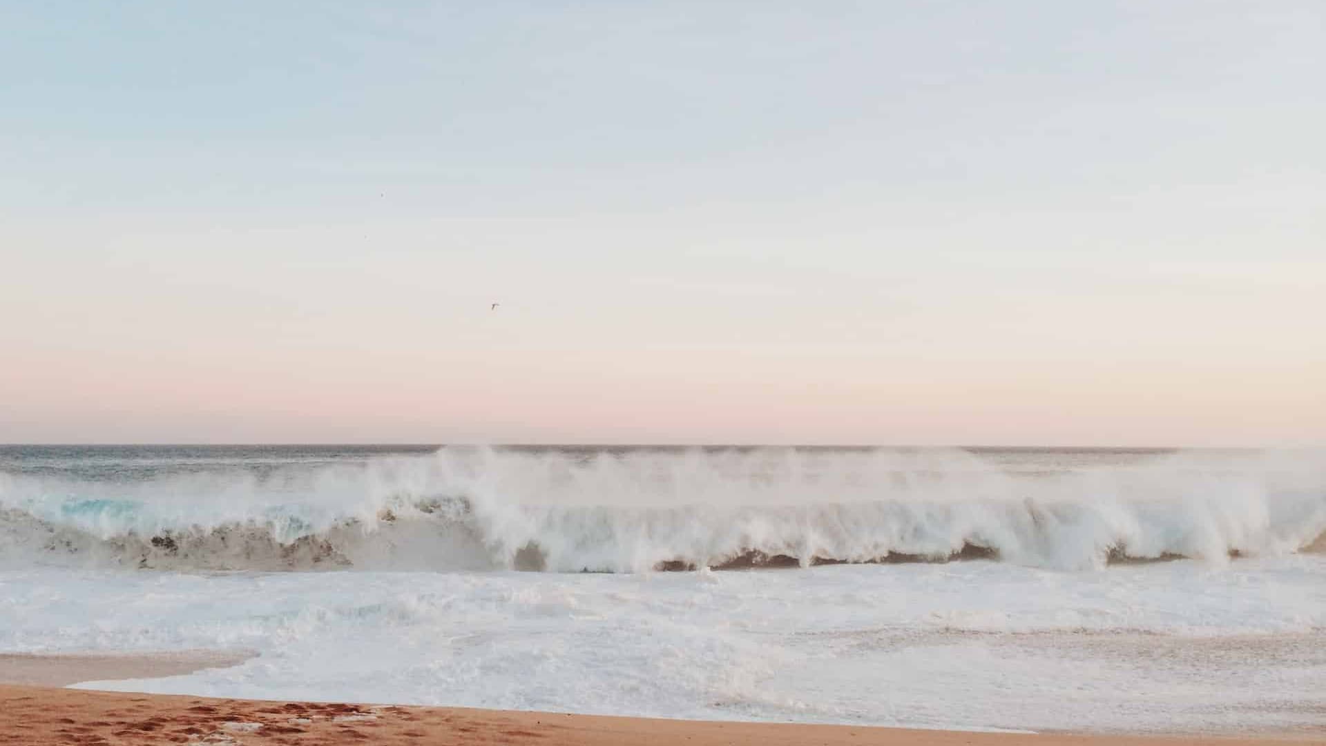 Waves crashing on a sandy beach under a pastel sky.