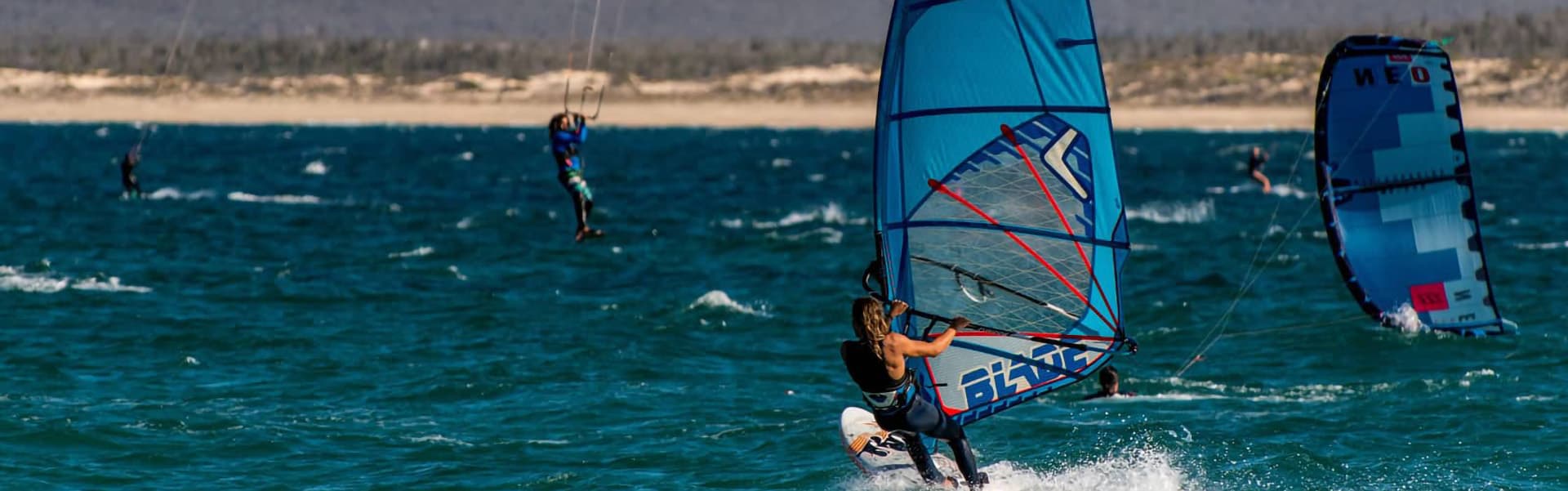 A windsurfer glides across the water with a colorful sail, surrounded by other water sports enthusiasts.